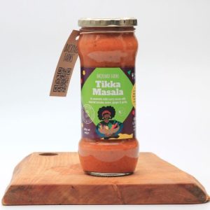 backyard farms tikka masala sauce in a glass jar sitting on a wooden board with a white background