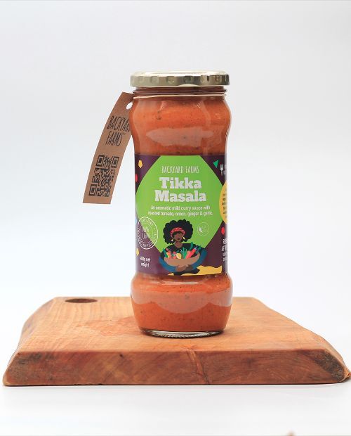 backyard farms tikka masala sauce in a glass jar sitting on a wooden board with a white background