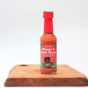 backyard farms mango chilli hot sauce in a glass bottle sitting on a wooden board with a white background