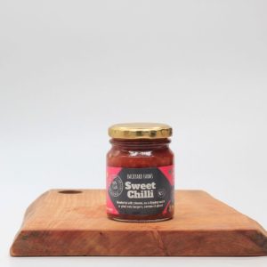 backyard farms sweet chilli sauce in a glass jar with a label sitting on a wooden board with a white background